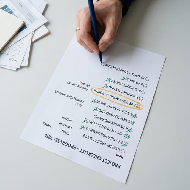 Hand ticking off items on a printed project checklist with an item awaiting sign-off circled in amber - the practical work of walking the NDIS certification audit list bucket by bucket.